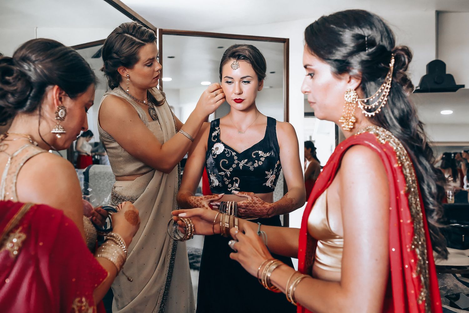 A group getting ready in traditional Indian wedding attire with saris and jewelry in a preparation room.