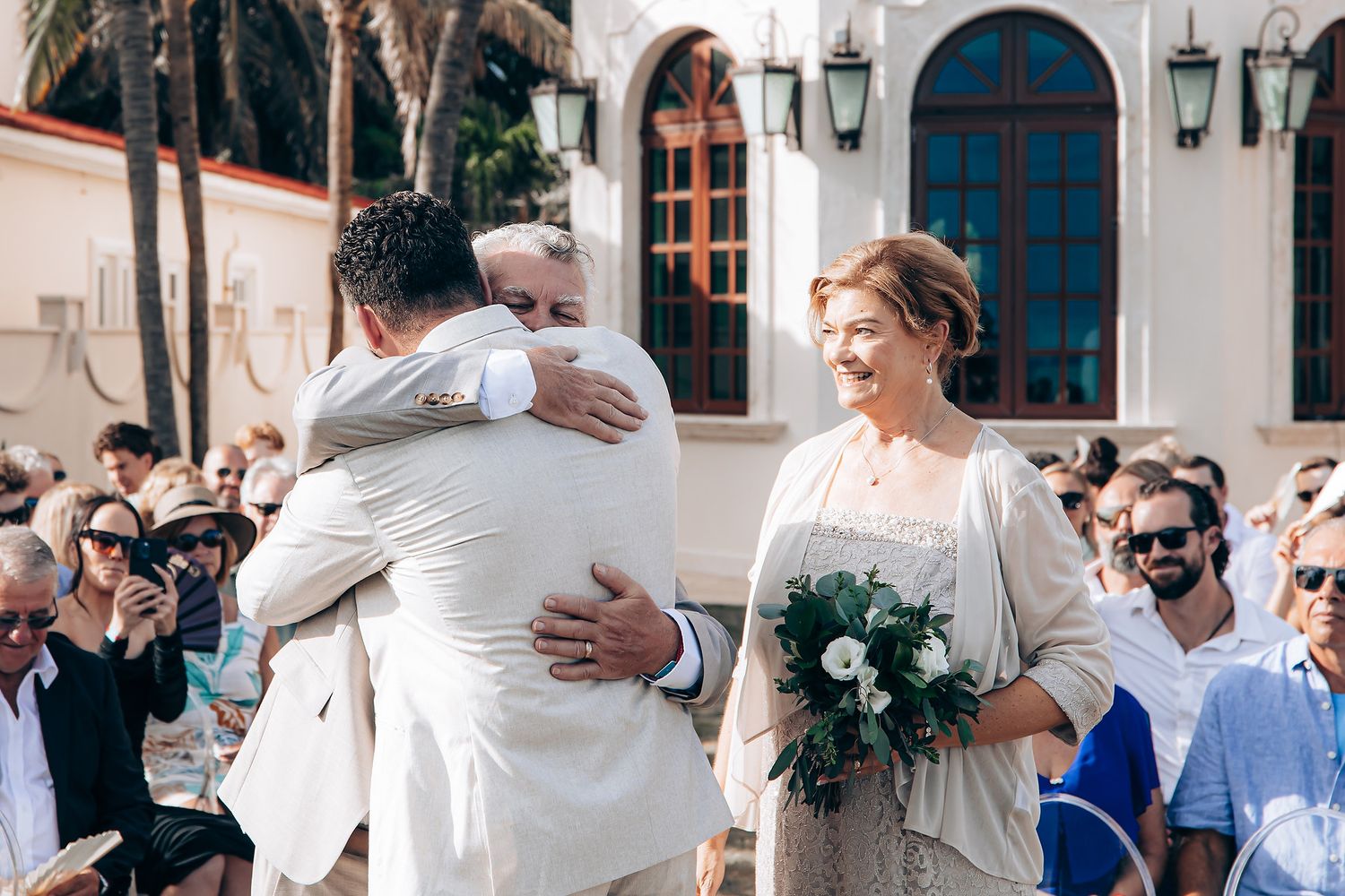 Wedding guests celebrate during an outdoor ceremony at a venue with elegant arched doors and white walls.