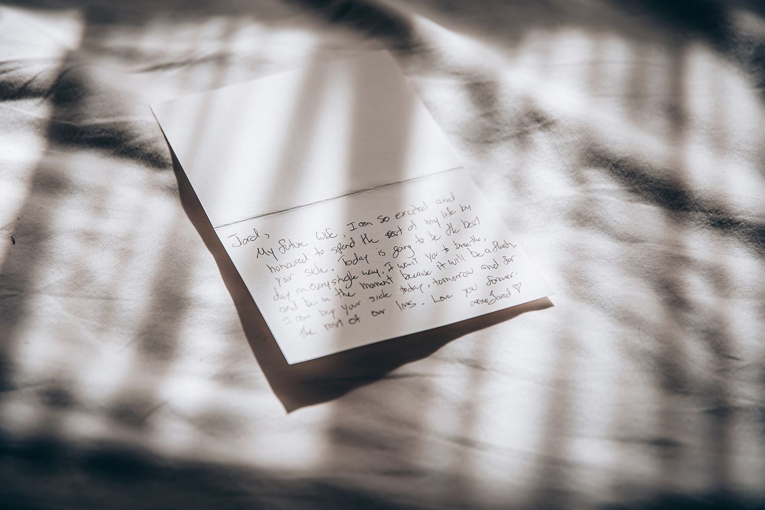 An open handwritten letter on white paper casts dramatic shadows in natural window light.
