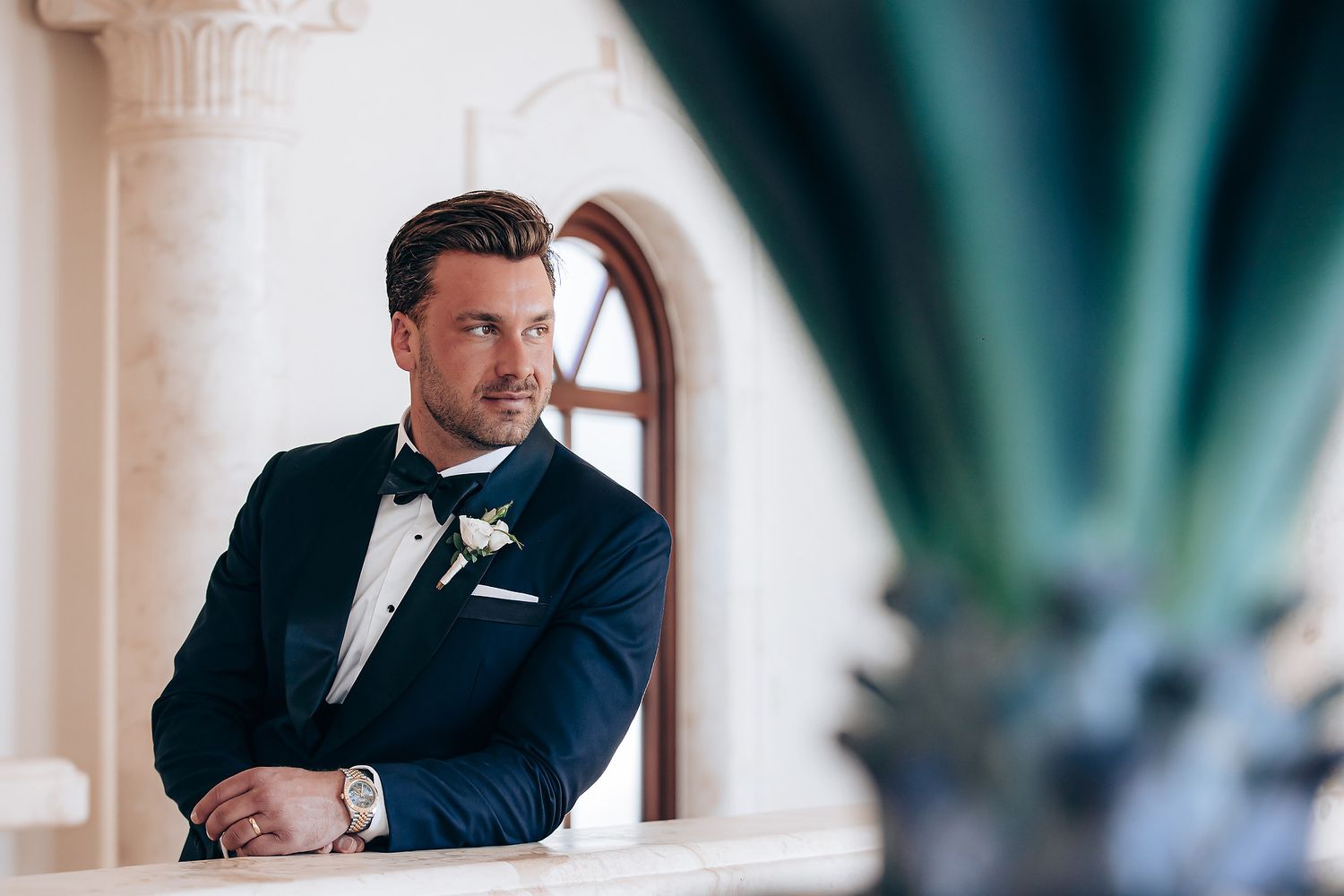 A couple shares an intimate moment in a classic black and white formal attire against a bright interior setting.