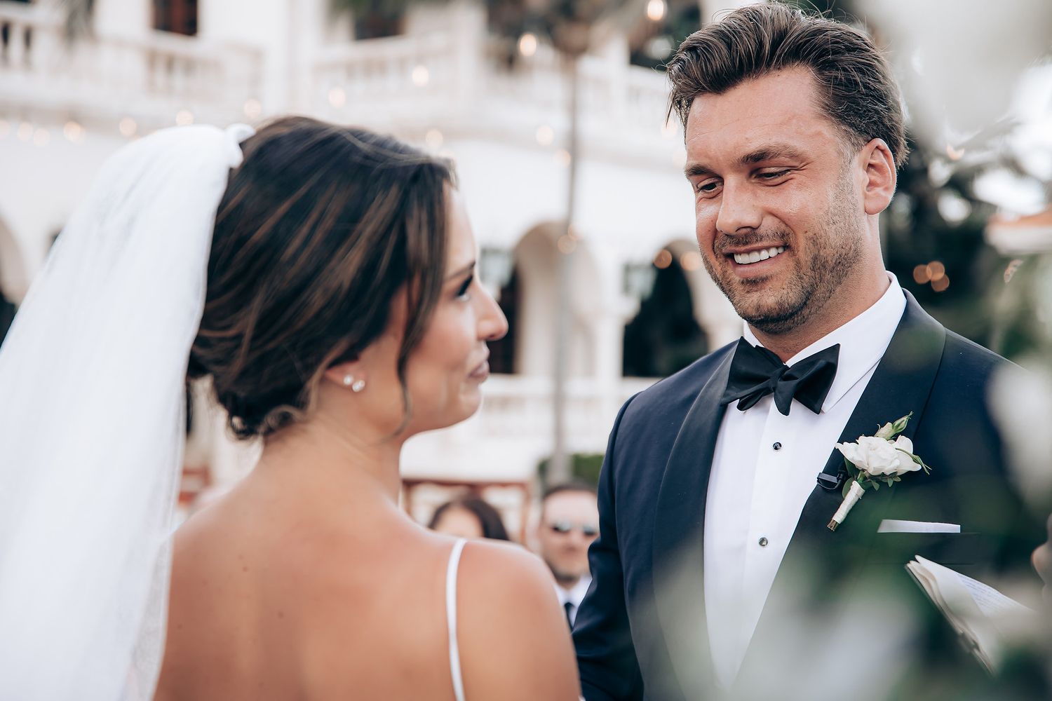 A romantic wedding ceremony moment captured under an elegant floral arch with white roses.