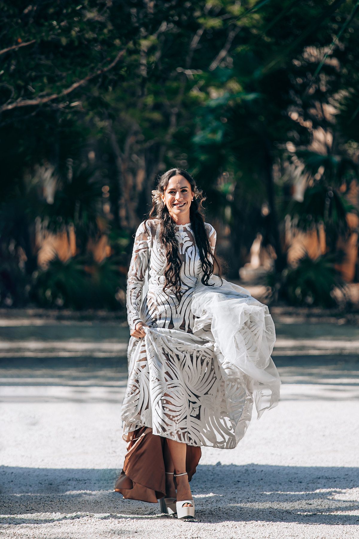 A flowing white patterned dress billows in the wind during an outdoor photoshoot with trees in background.