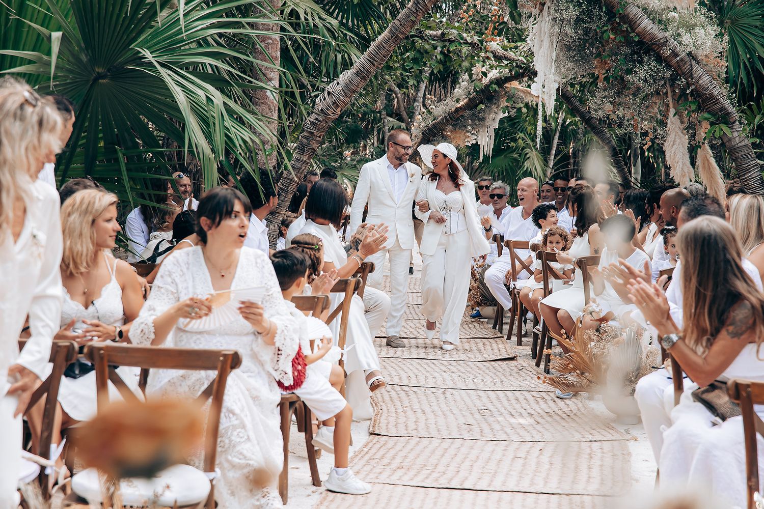 Large group of people dressed in white gather outdoors for a tropical celebration or event.