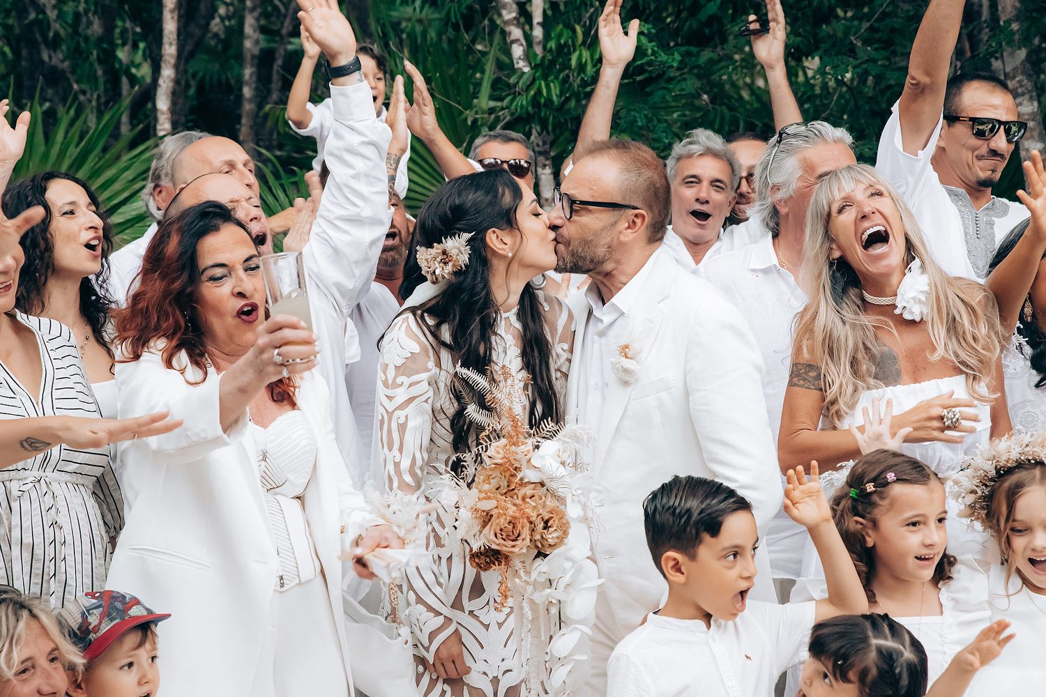 Enthusiastic wedding guests cheer and celebrate during an outdoor reception.