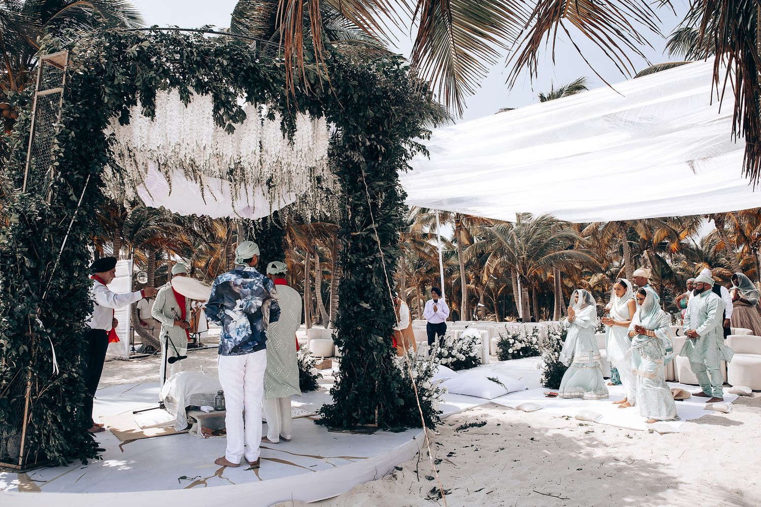 Panoramic view of wedding guests gathered for an outdoor ceremony under palm trees.