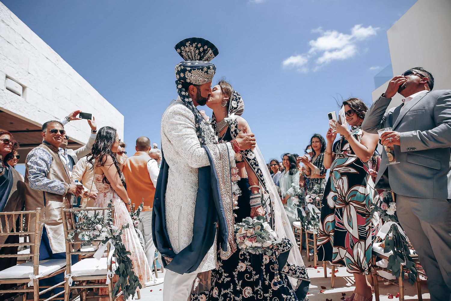 Wedding guests gather outdoors for a celebratory moment under clear blue skies.