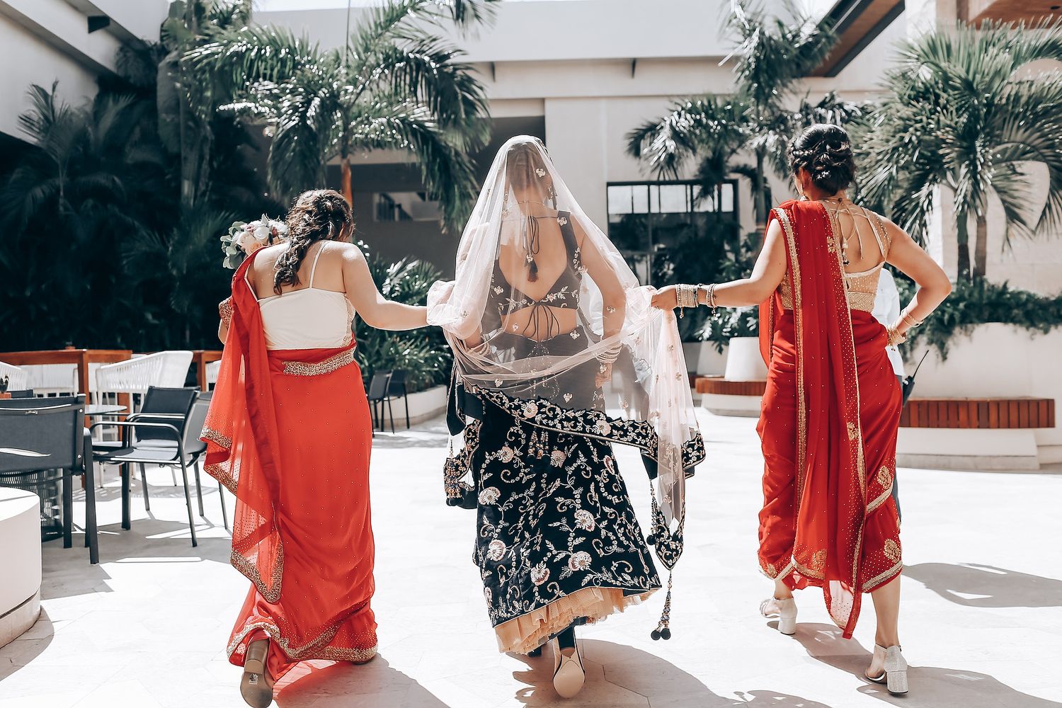 Bridesmaids in coral dresses pose together at a beachside wedding venue.