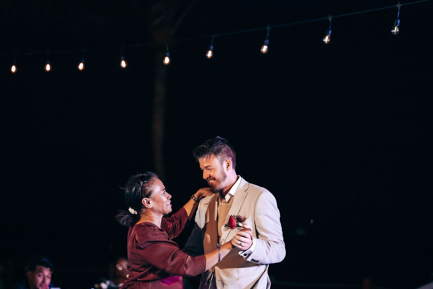 Wedding reception dance floor lit by overhead string lights at night.