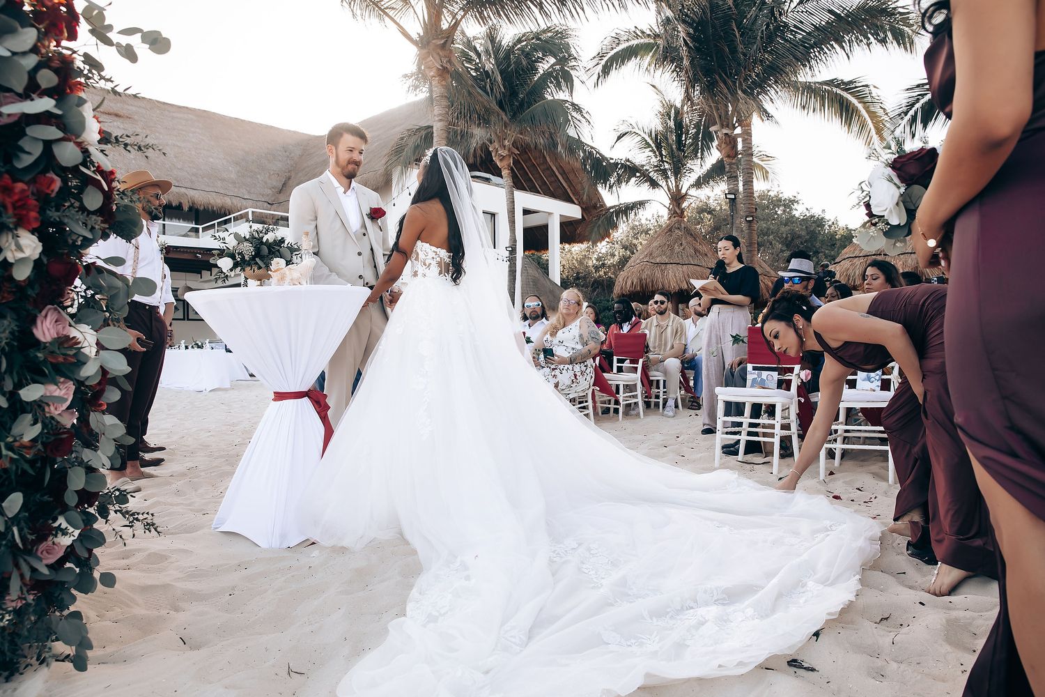 A beach wedding ceremony setup with white chairs and tropical palm trees along the shoreline.