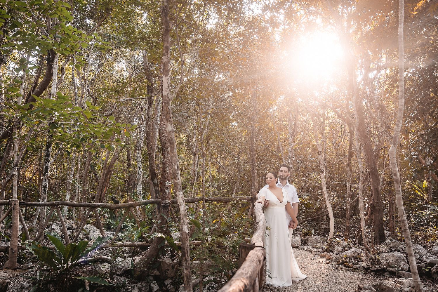 Sunlit portrait of couple in white attire among tropical forest setting.