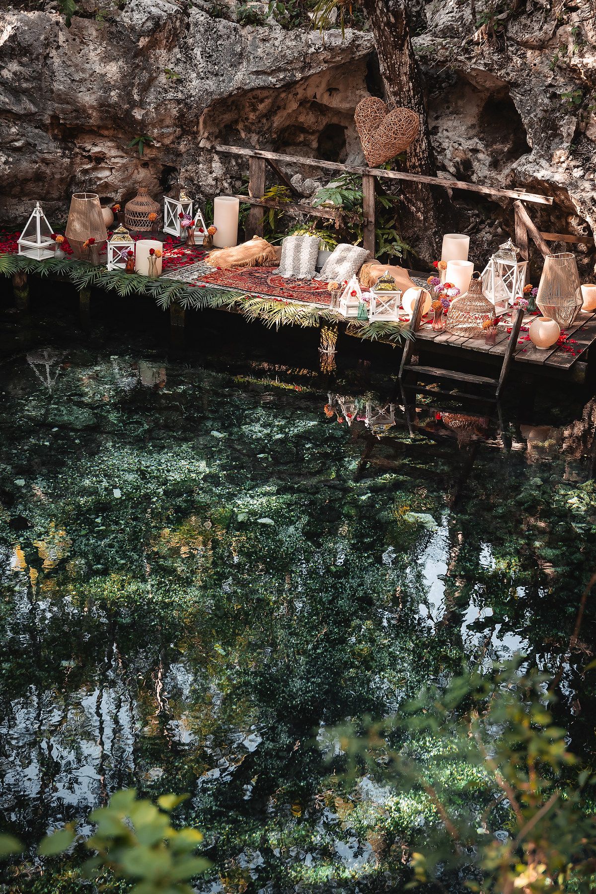 A tranquil cenote with turquoise water reflecting lush vegetation and rocky formations along the edge.