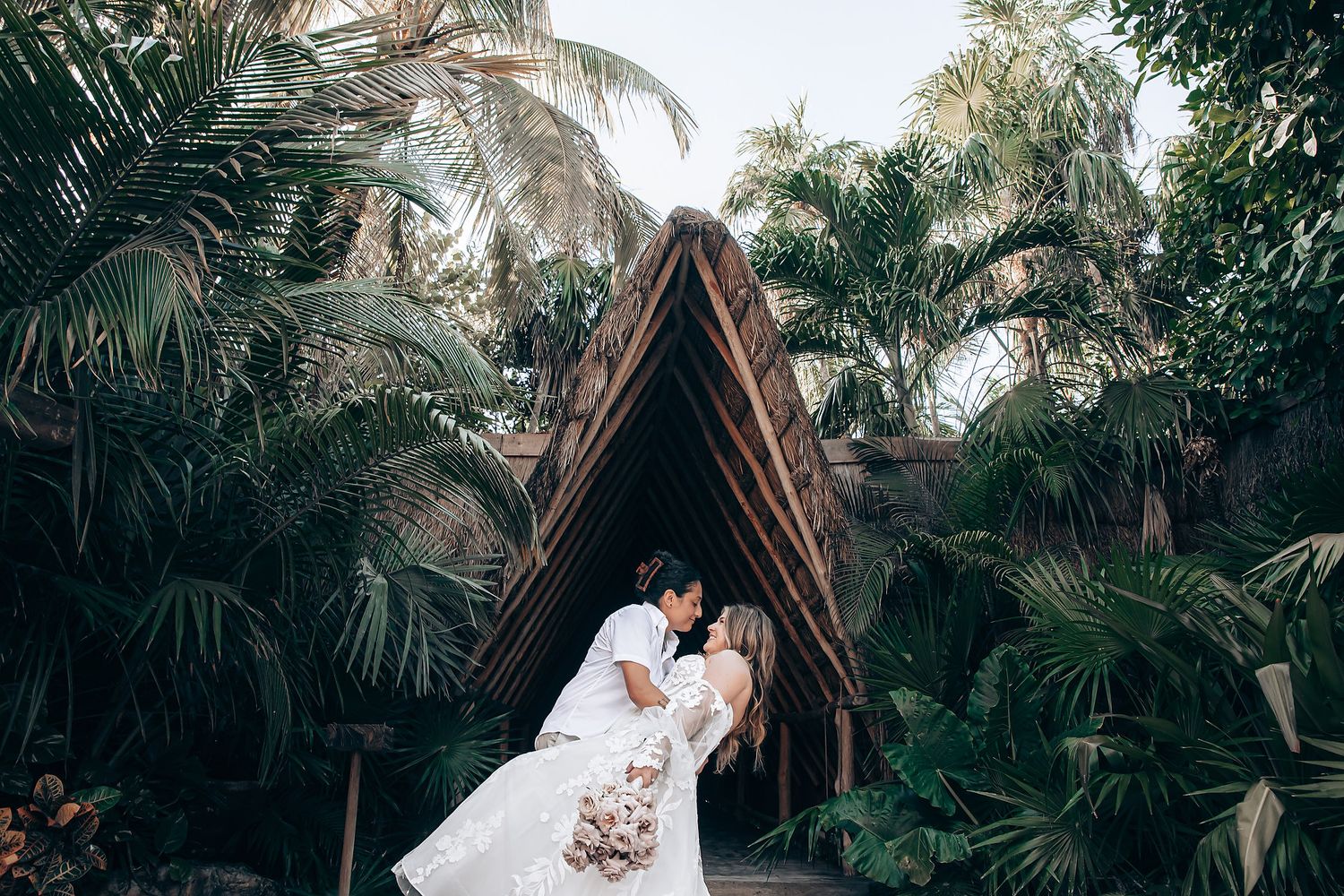 A couple embraces during their tropical beach wedding ceremony surrounded by palm trees and ocean views.
