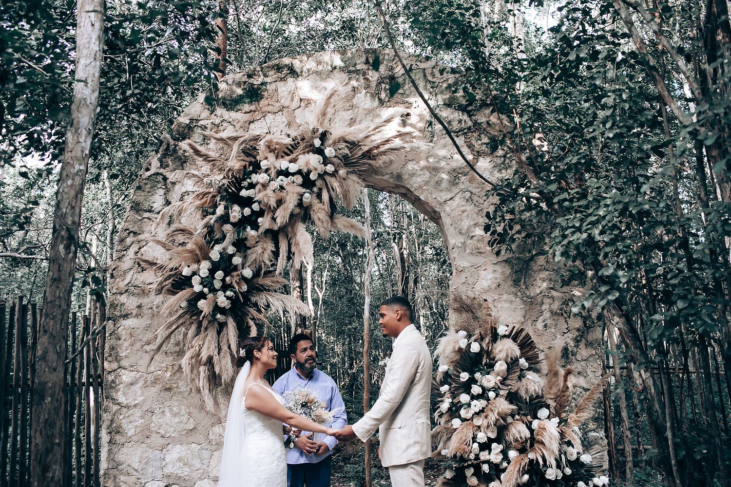 A romantic wedding ceremony takes place in a sunlit forest with natural decor and floral arrangements.
