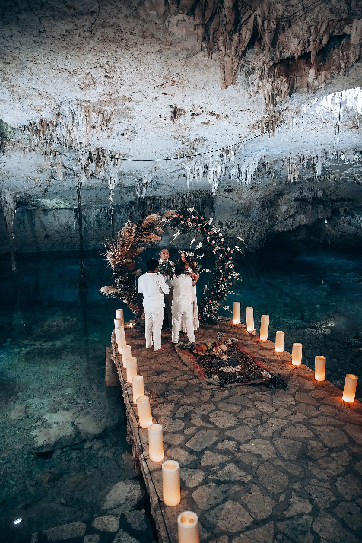 A romantic ceremony setup in a cenote cave with glowing candles along a stone path and turquoise water below.