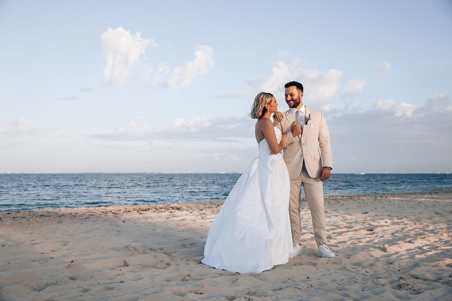 A romantic beach wedding photo sequence showing a couple in white attire walking along the sandy shoreline at sunset.