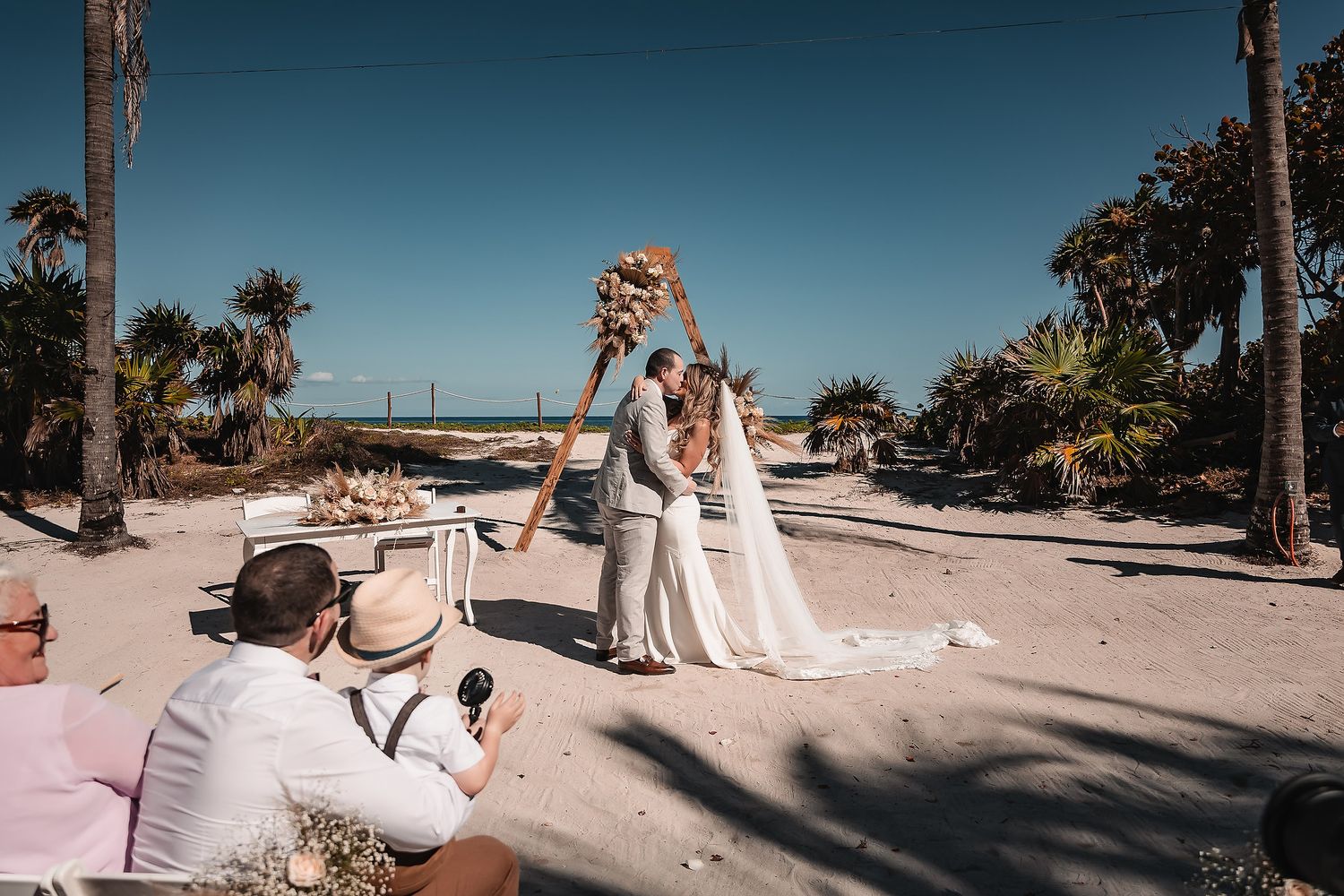 Panoramic view of a beach wedding setup with palm trees and white decor.