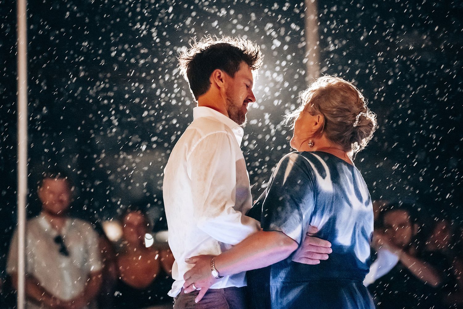 Wedding couple dances in falling snow during an evening celebration.