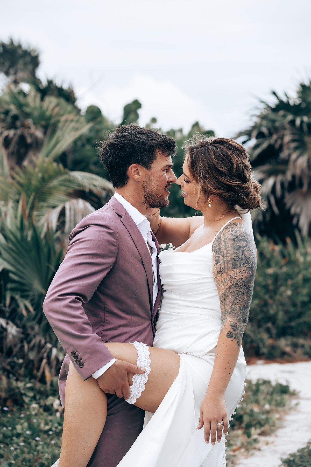 Wedding couple embraces on a tropical beach surrounded by palm trees.