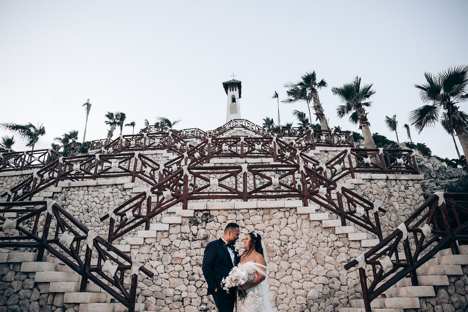 Couple sharing a romantic moment on grand stone steps with palm trees in the background.