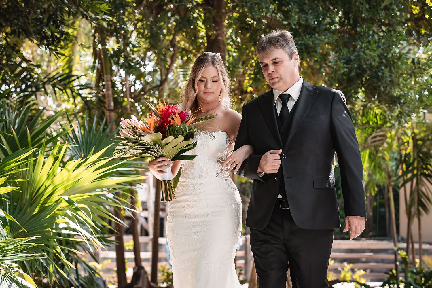 Wedding couple walking together on stone pathway surrounded by tropical foliage.