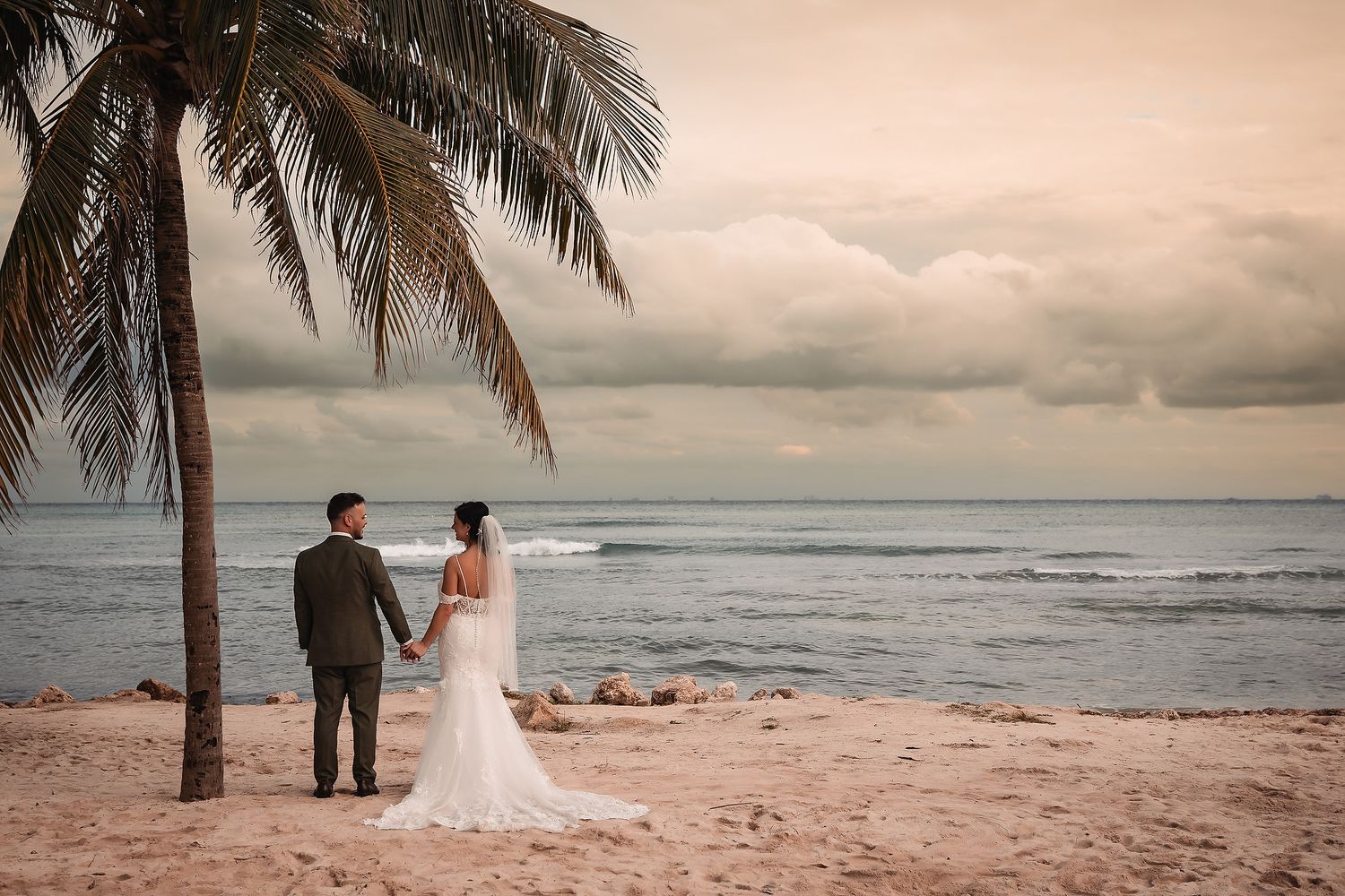 Romantic beach wedding scene with palm trees and ocean waves at sunset.