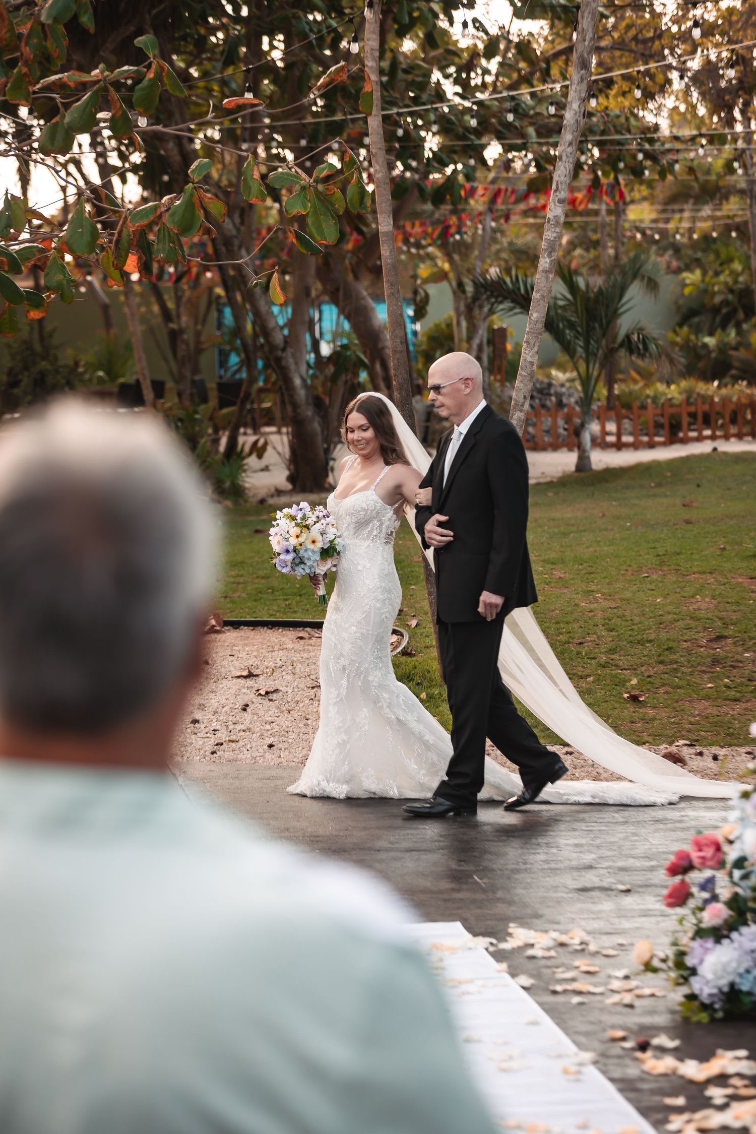 Wedding ceremony processional on a stone pathway surrounded by lush gardens.