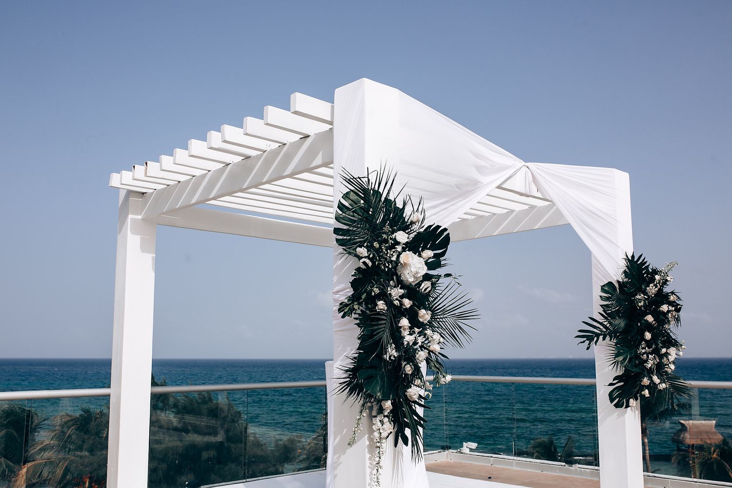 Elegant white wedding arch and chairs set up on a beachfront terrace with ocean views.