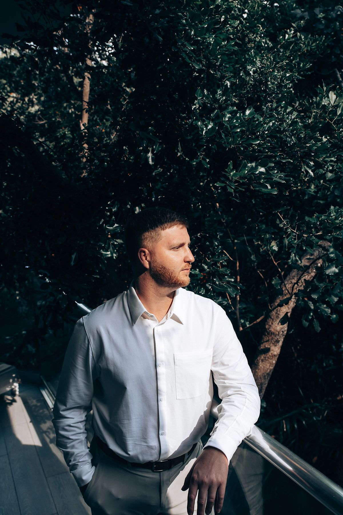 Person in white shirt seated outdoors against lush green foliage backdrop.