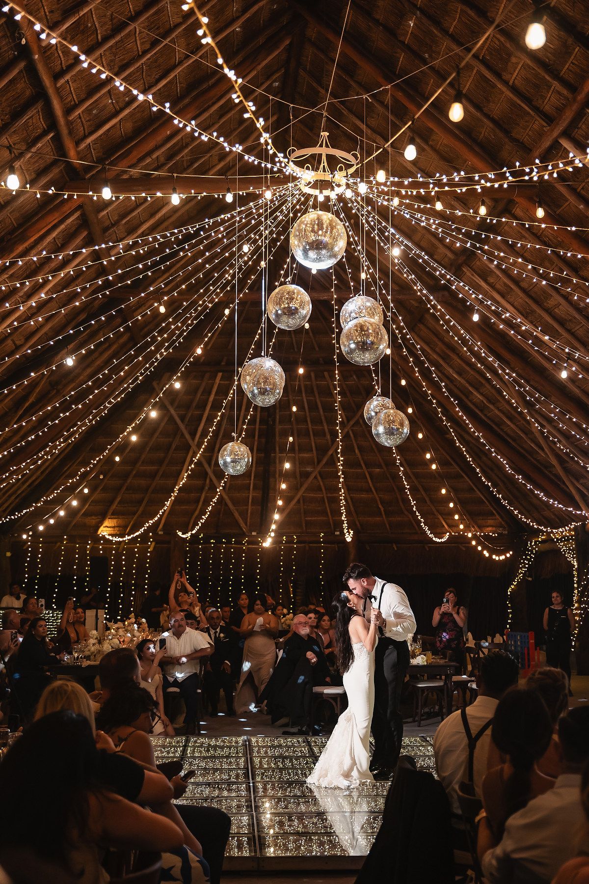Wedding guests watch a couple's first dance under magical string lights and disco balls.