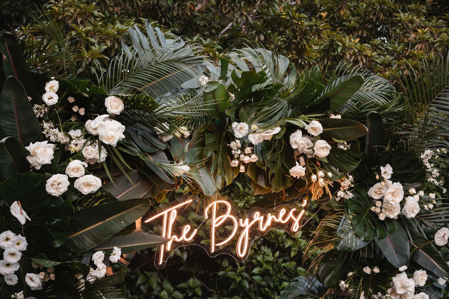 Elegant wedding reception decor with white flowers and tropical greenery.