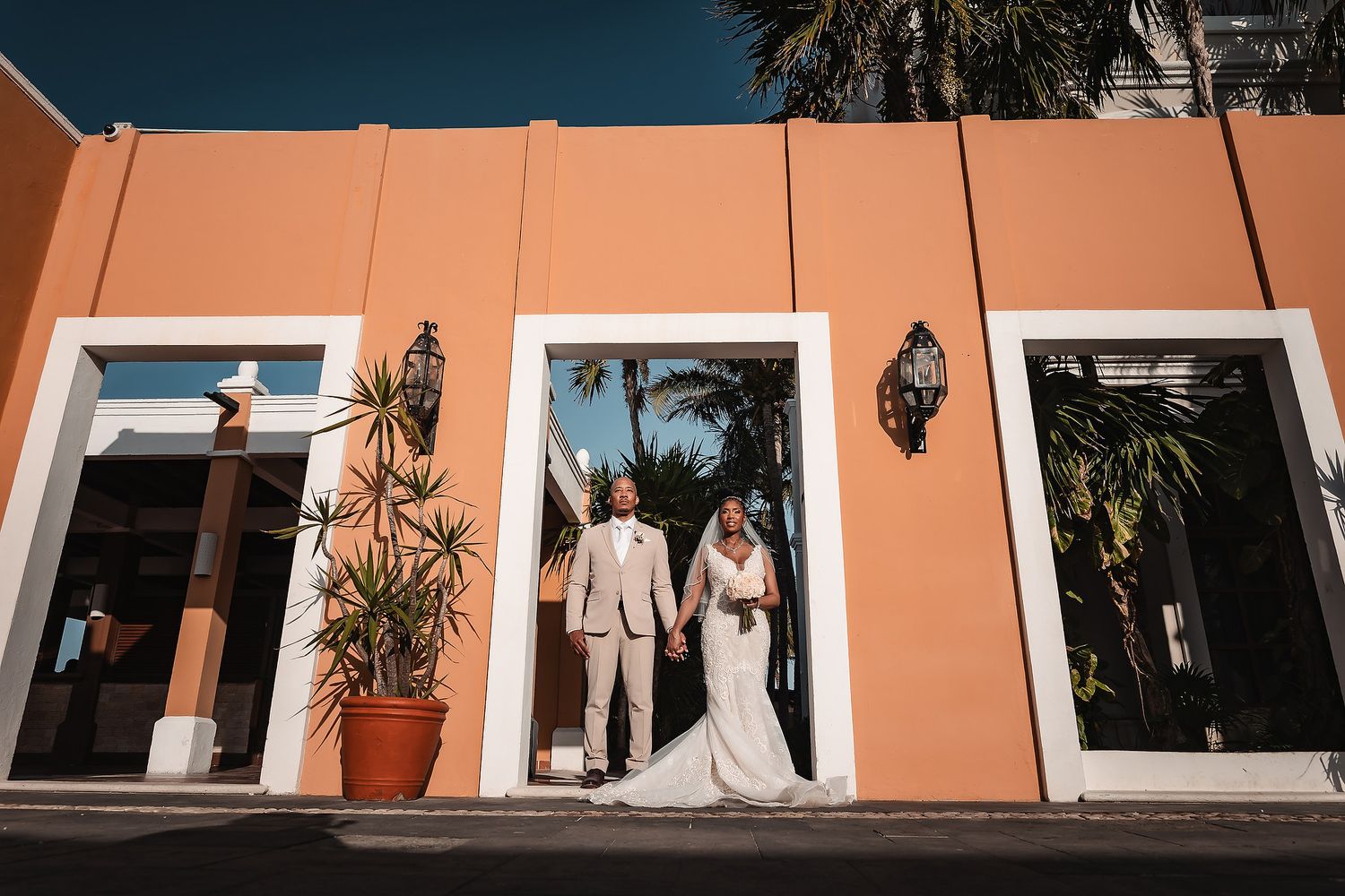 Palm trees line a walkway against a peach-colored wall at a tropical wedding venue.