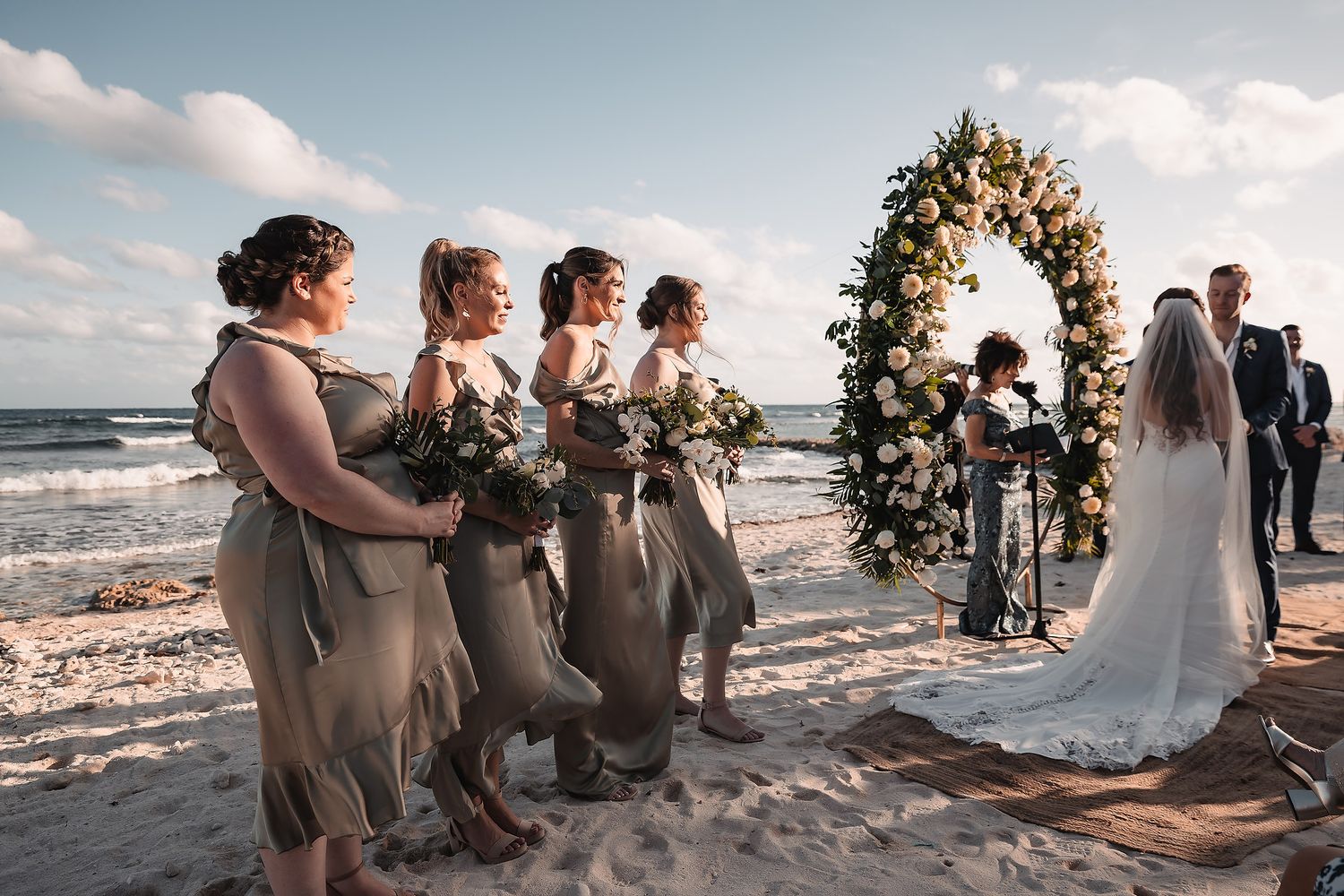 Wedding party in neutral tones gathered on beach during sunset ceremony.