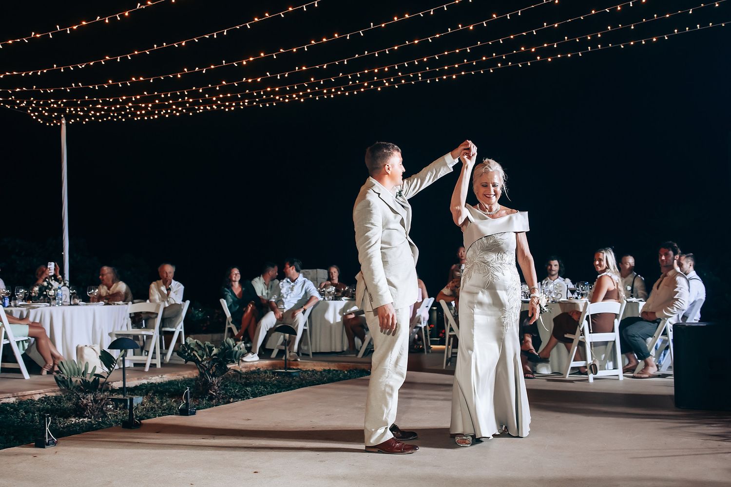 Evening wedding reception under string lights with guests dancing.