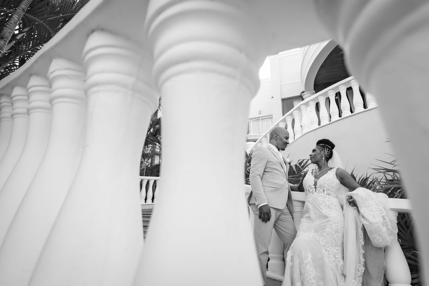Black and white wedding photo of bride and groom standing between white columns at elegant venue.