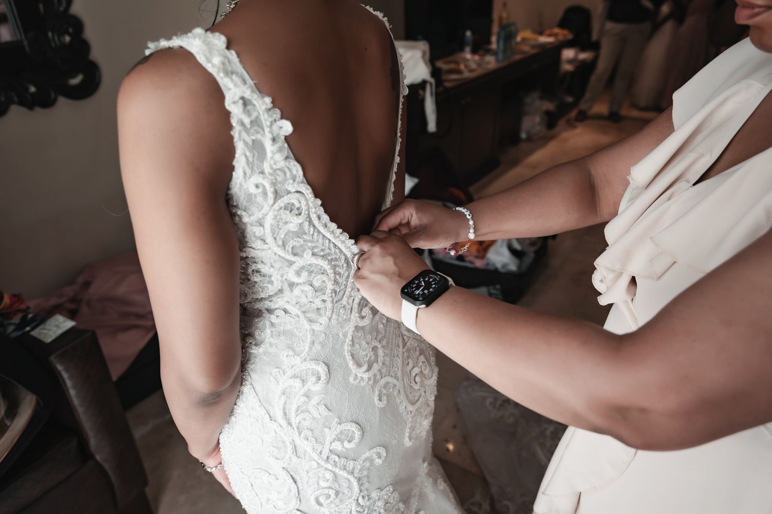 Close-up of bridesmaid fastening buttons on back of white lace wedding gown.
