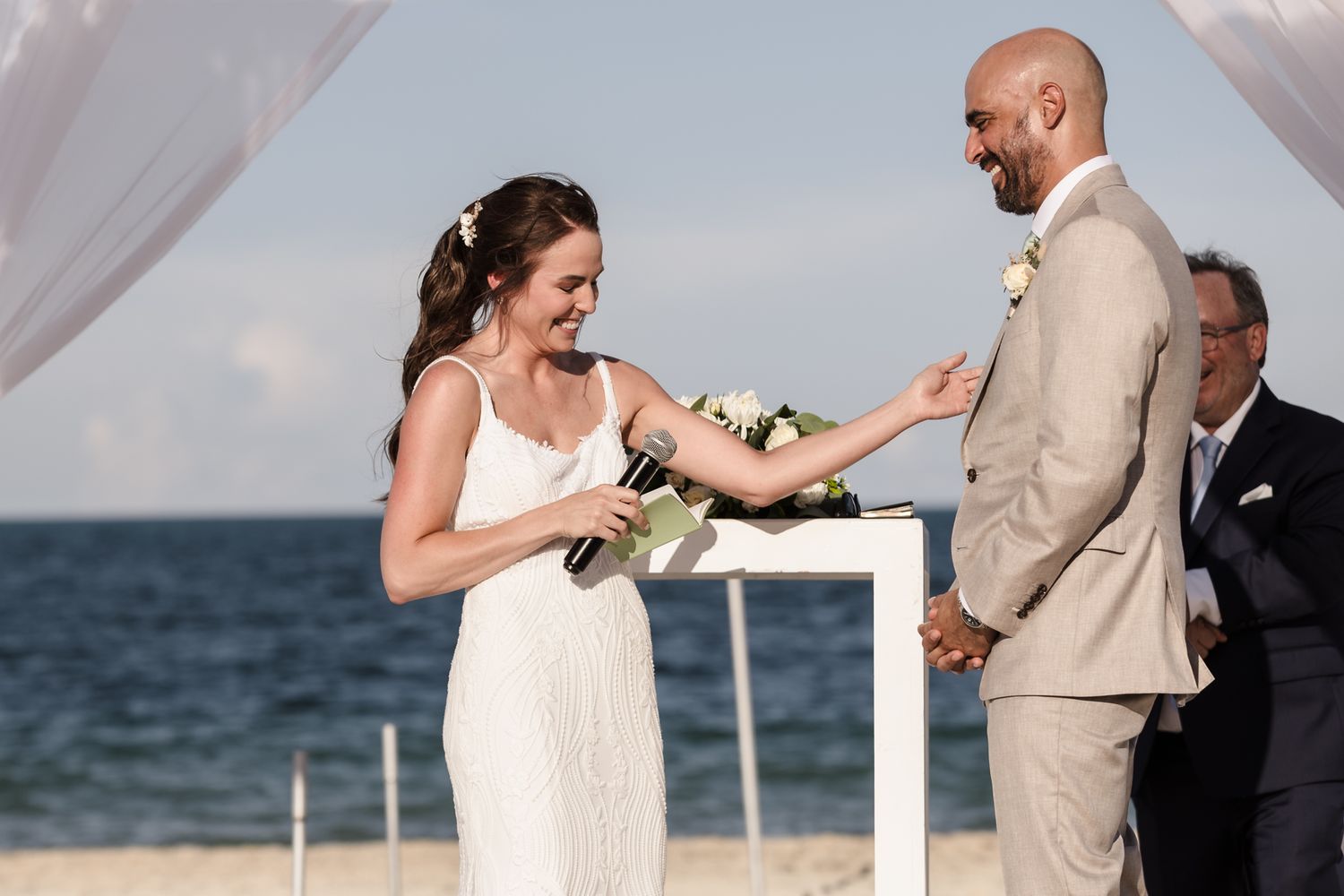 Bride and groom exchanging rings during a romantic beach wedding ceremony with ocean backdrop.