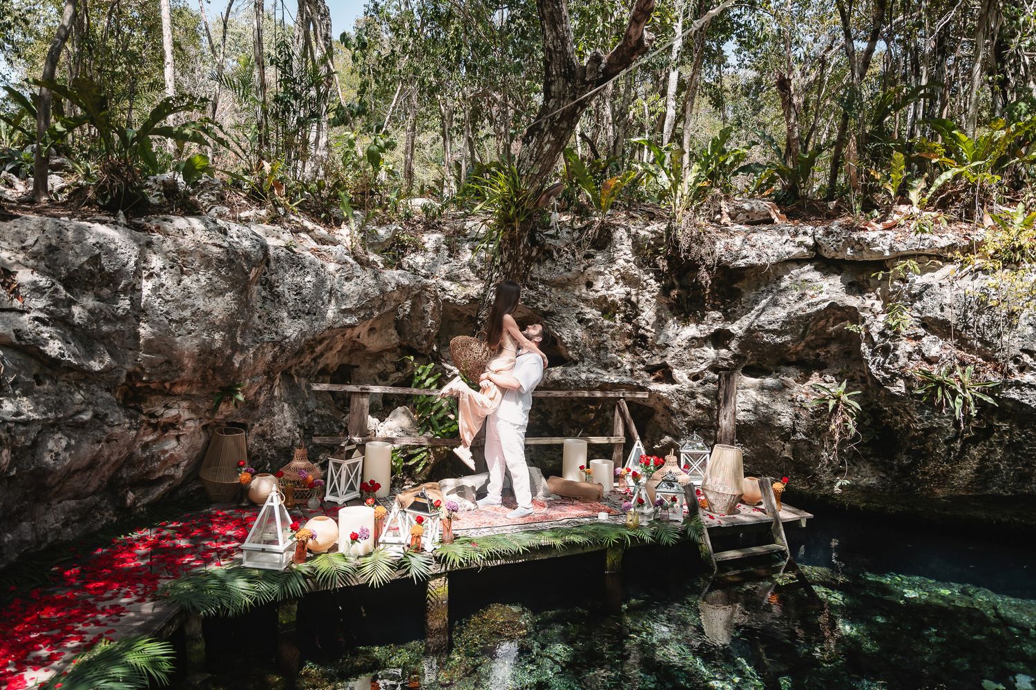 Couple embracing on a decorated dock over a crystal-clear cenote surrounded by lush jungle in Mexico.