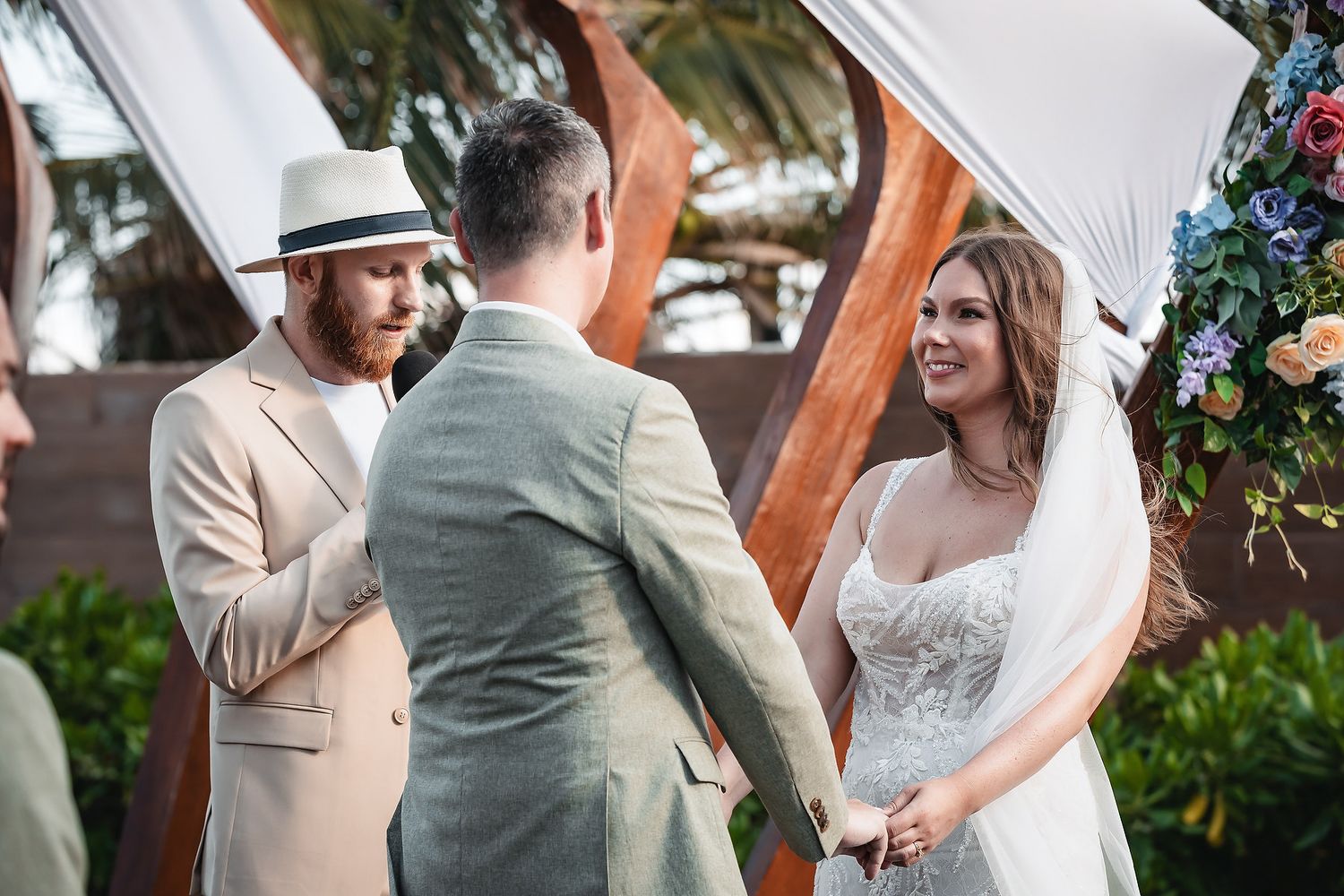 Couple exchanging vows at outdoor wedding ceremony with officiant and floral arch backdrop.