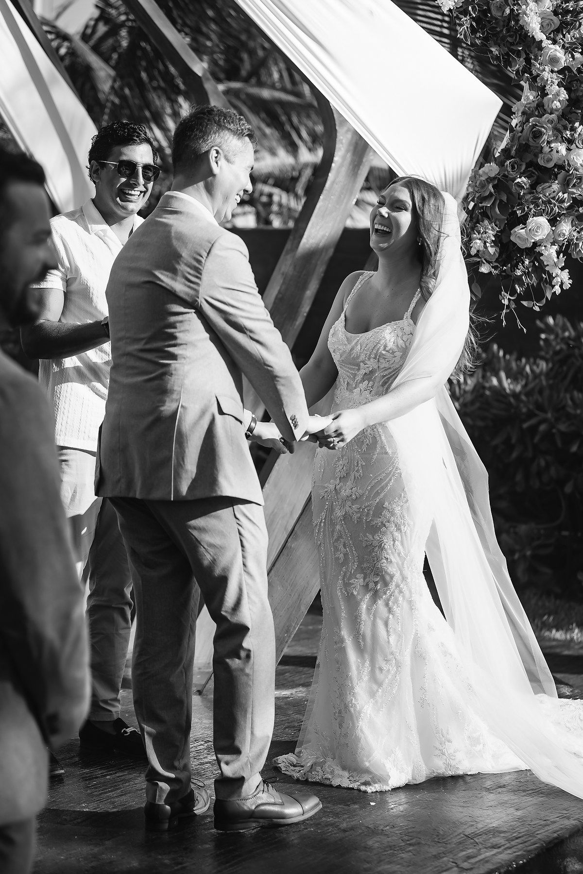 Black and white photo of a laughing bride and groom holding hands at their outdoor wedding ceremony.