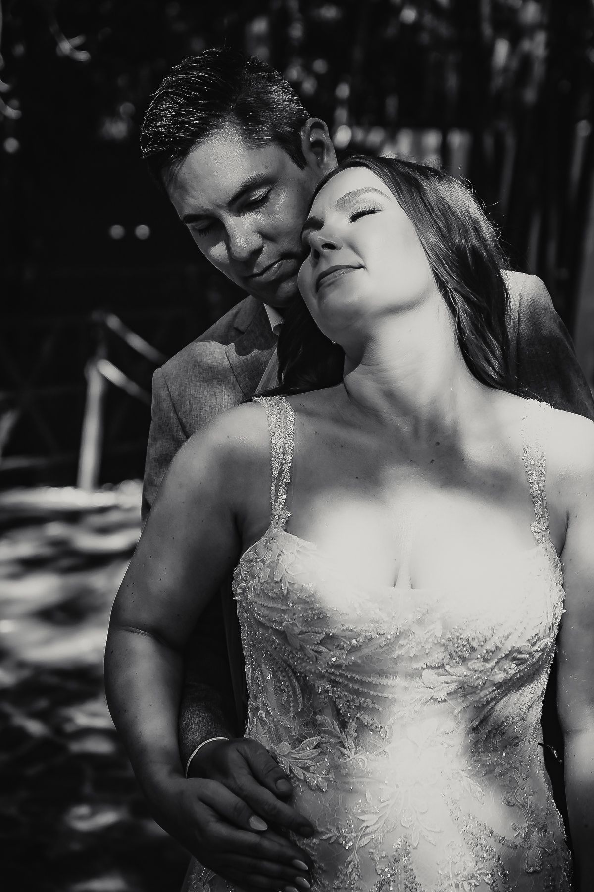 Black and white photo of a bride and groom sharing a tender moment outdoors, groom kissing bride's cheek.