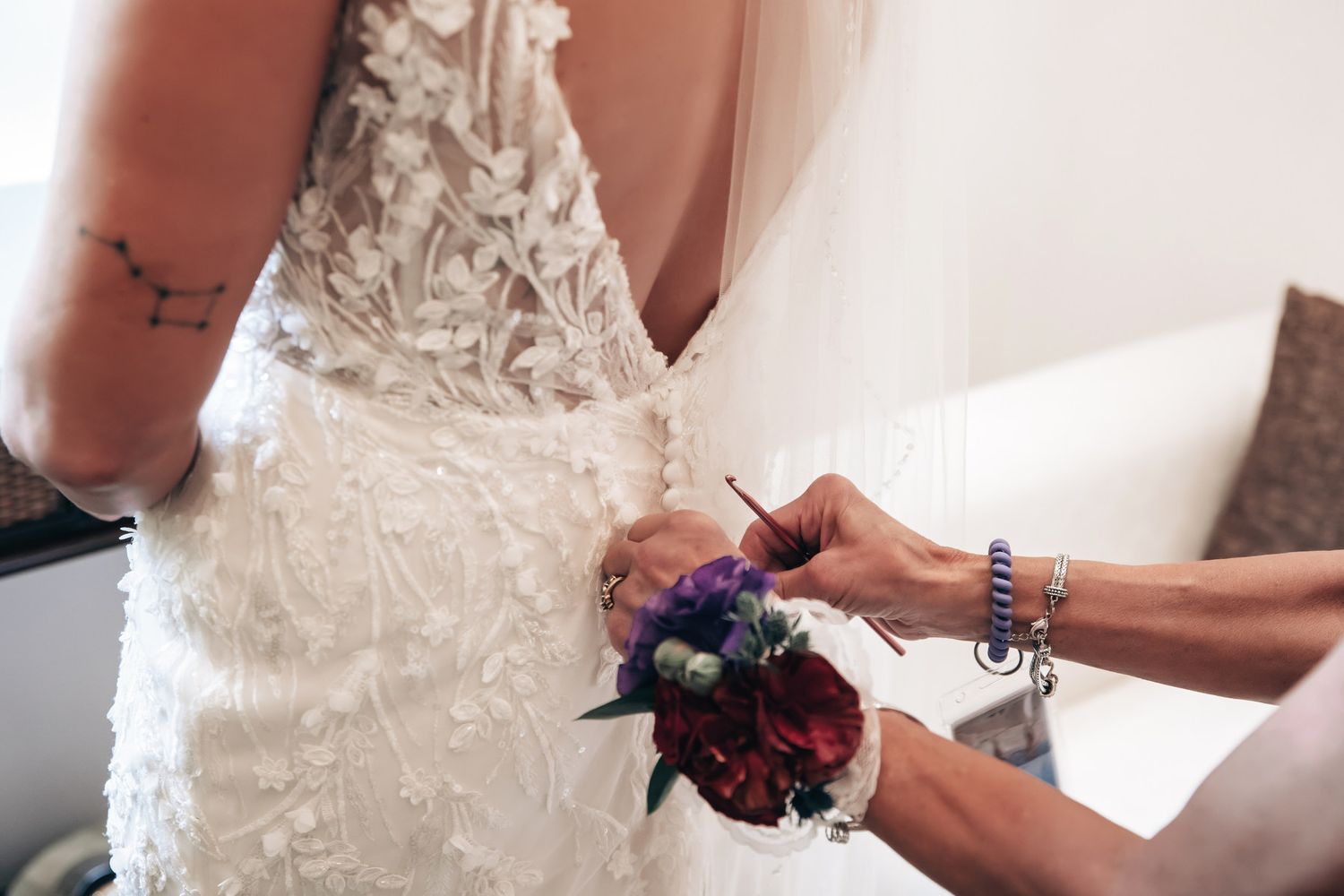 Close-up of hands fastening buttons on a bride's intricate lace wedding dress with a floral corsage.