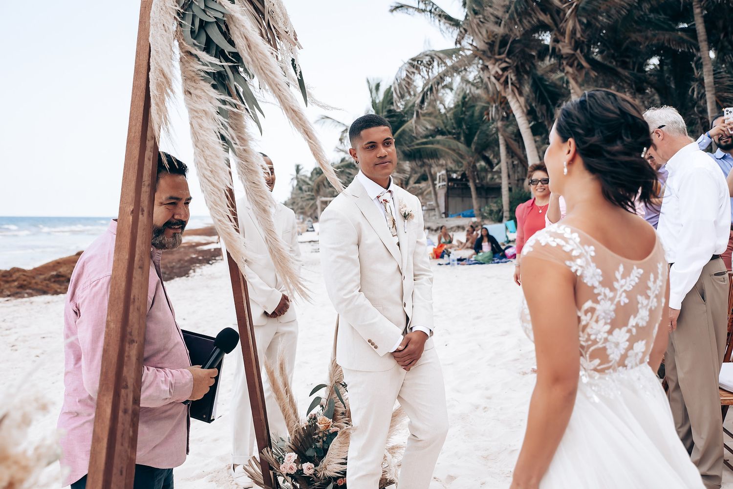 A tropical beach wedding ceremony with palm trees and guests gathered on the sand.