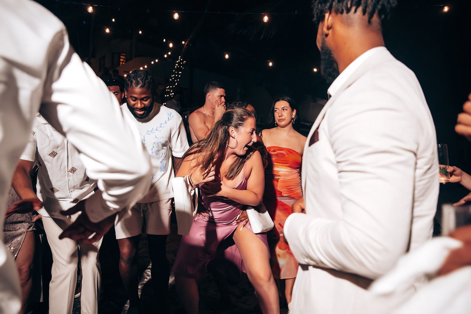 An energetic wedding reception dance party with guests in summer attire.