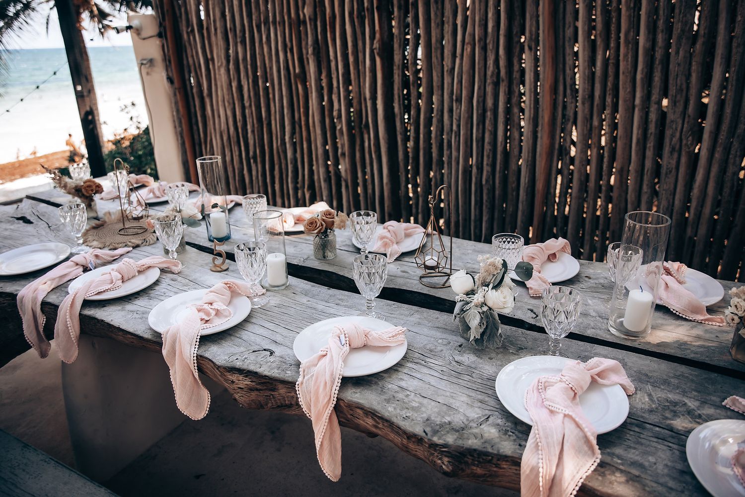 Elegant beach wedding reception tables decorated with blush linens and natural elements under palm trees.