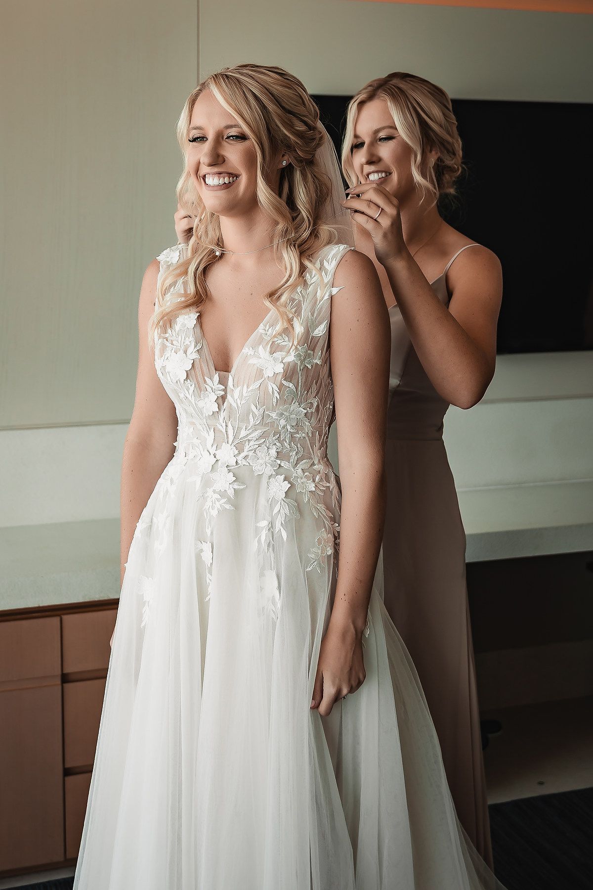 A flowing white wedding gown with lace bodice being adjusted in a bridal preparation room.