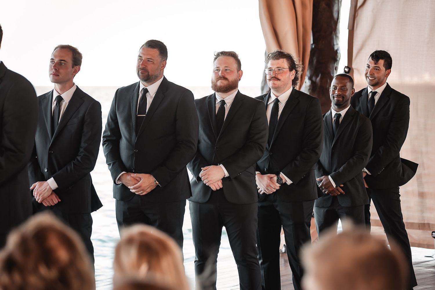 Groomsmen in black suits stand together during a formal wedding ceremony.