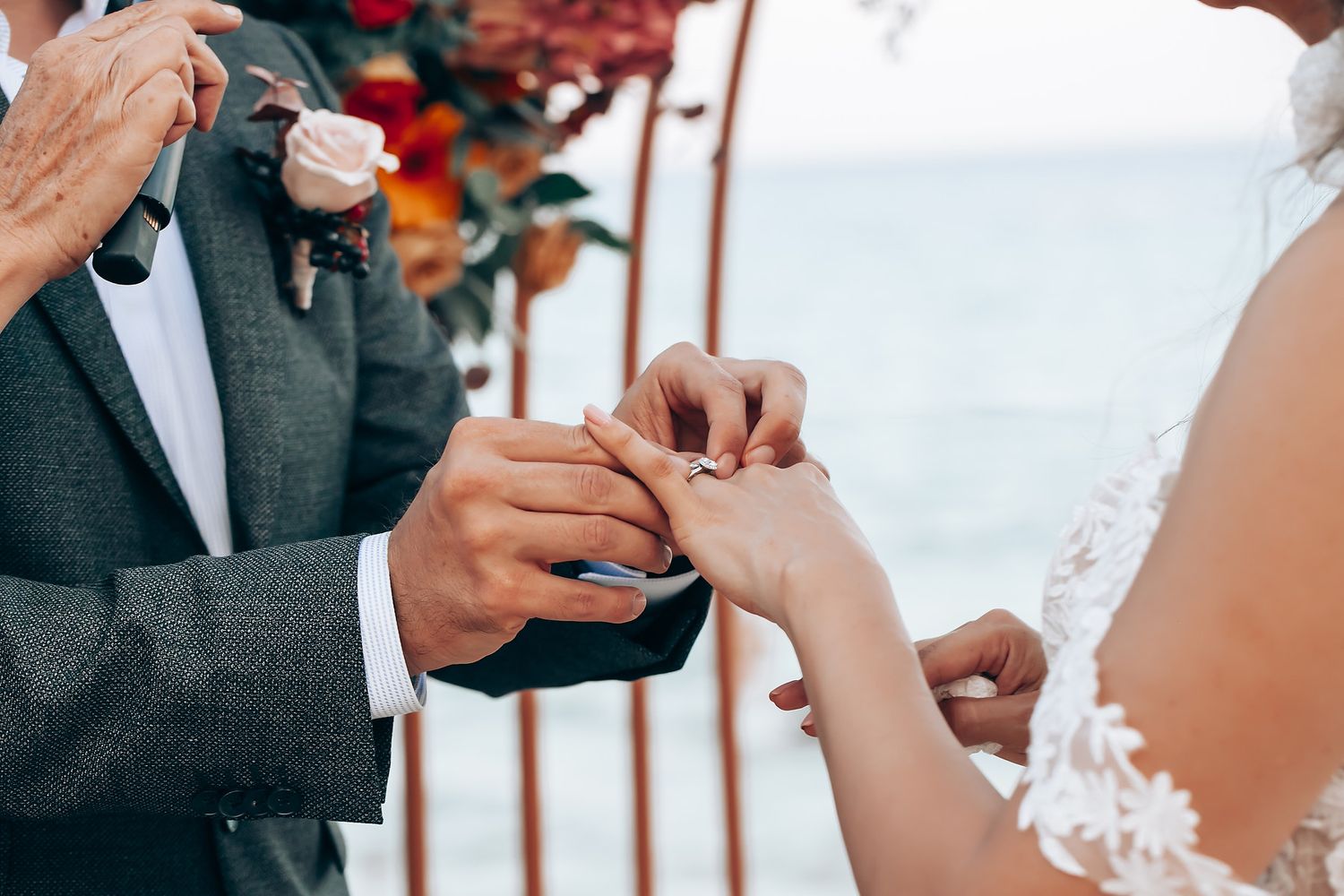 Hands exchanging wedding rings during an intimate ceremony with floral decor.