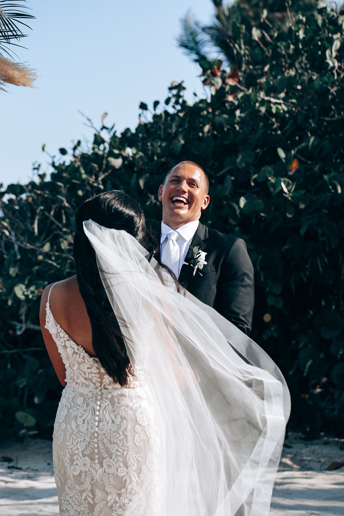 A flowing white lace wedding dress catches the sunlight against tropical foliage.