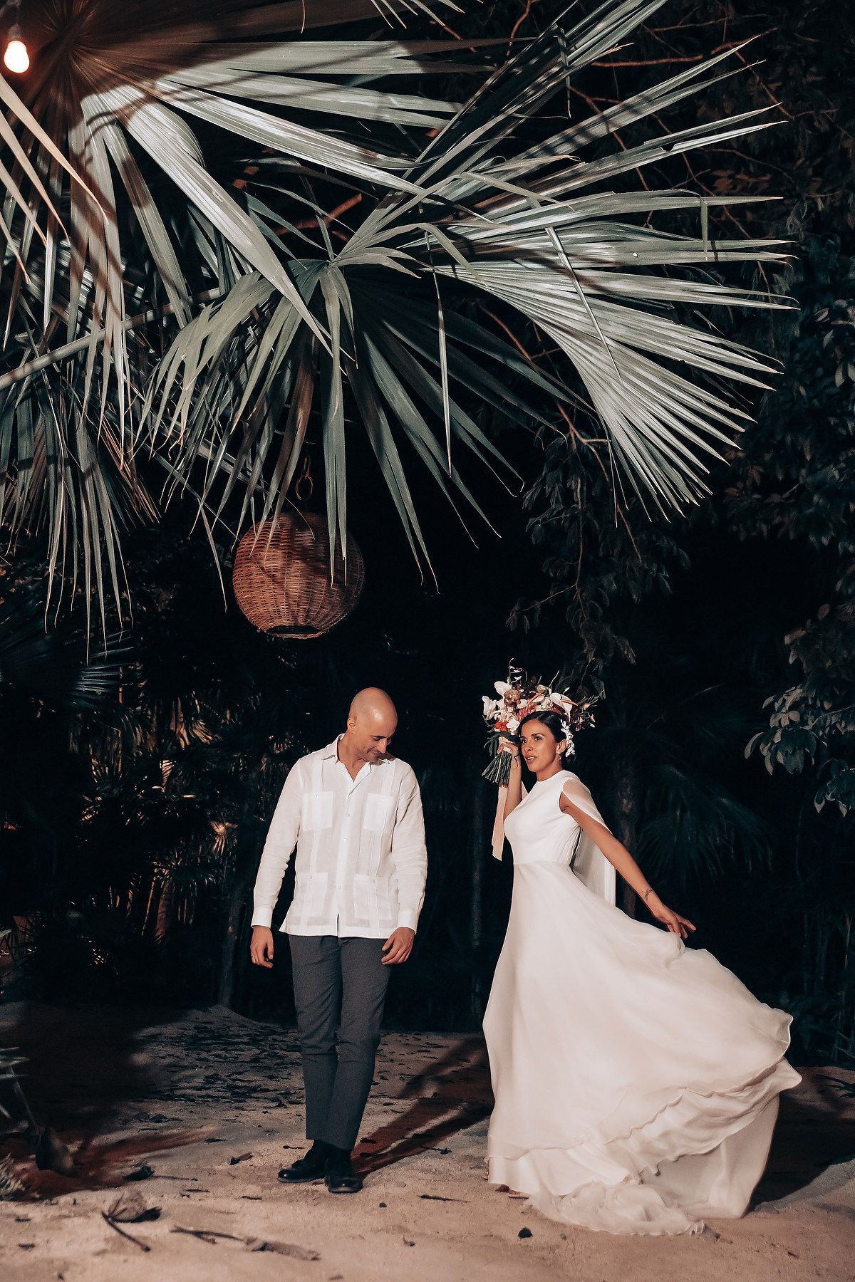 Couple dancing under palm trees in an intimate nighttime wedding setting.