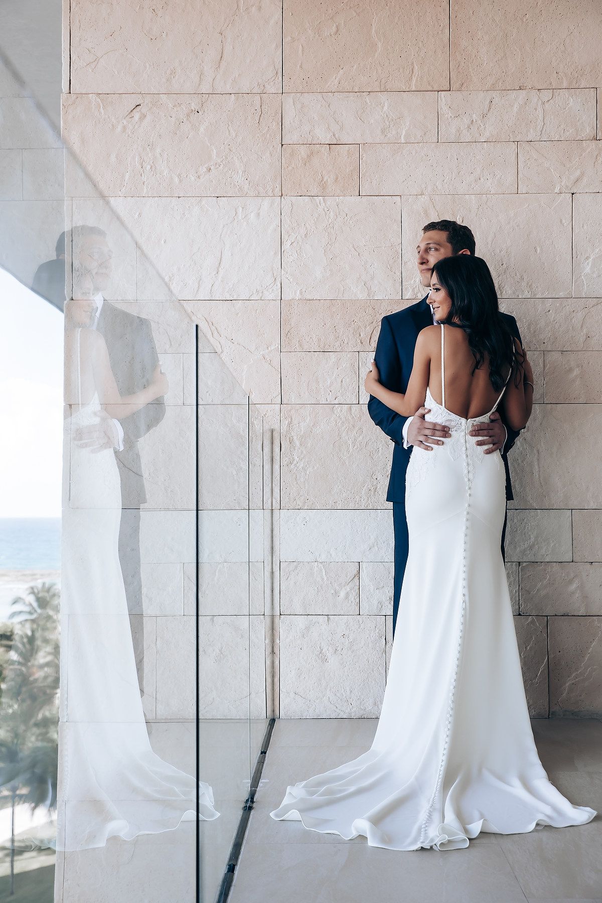 Romantic first look moment between couple against white stone wall with ocean view.